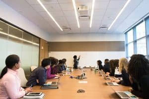 A woman that is in a board room presenting something to a group of other women.