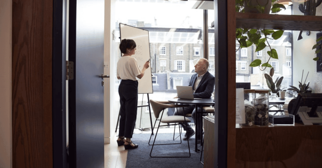 HR department man sitting and woman standing in front of white board explaining something