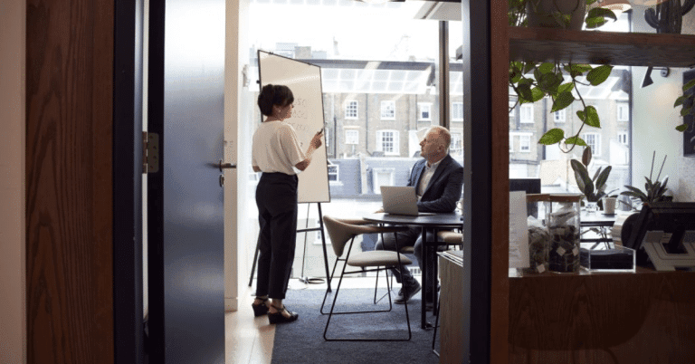 HR department man sitting and woman standing in front of white board explaining something