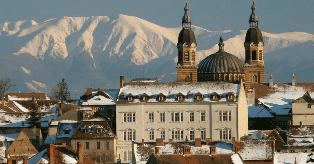 A picture of a place in romania with in the background mountains with snow on them
