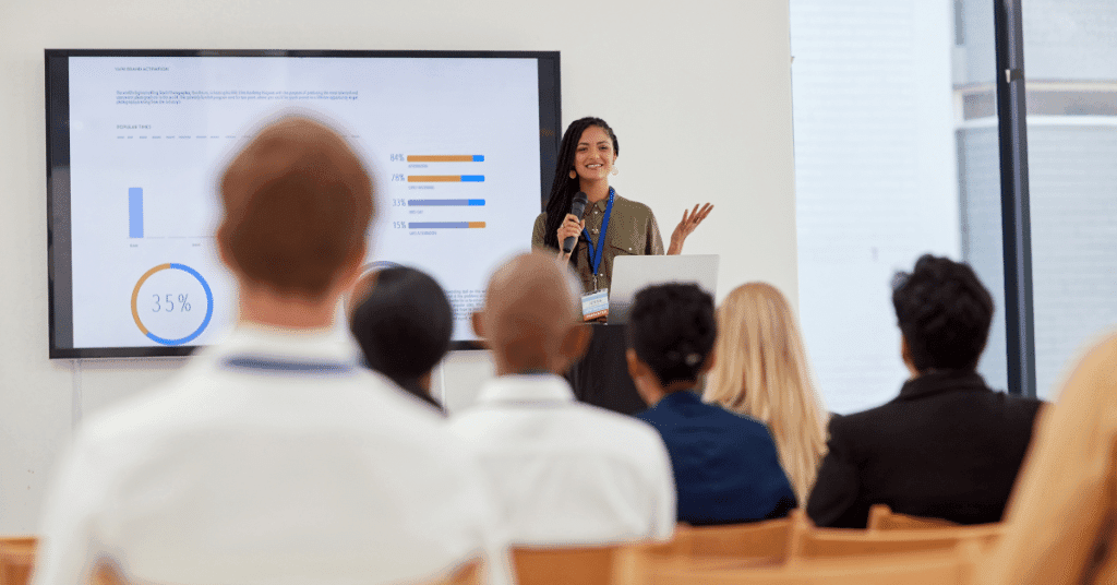 A woman in front of people giving a presentation on some data