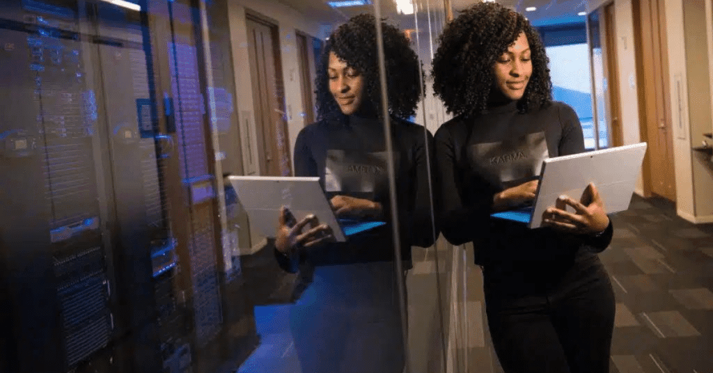 A woman standing with a small open laptop in a hallway