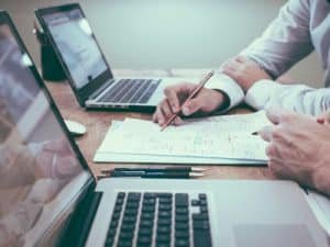 Two people with laptop and paper working on something together looking at the paper.