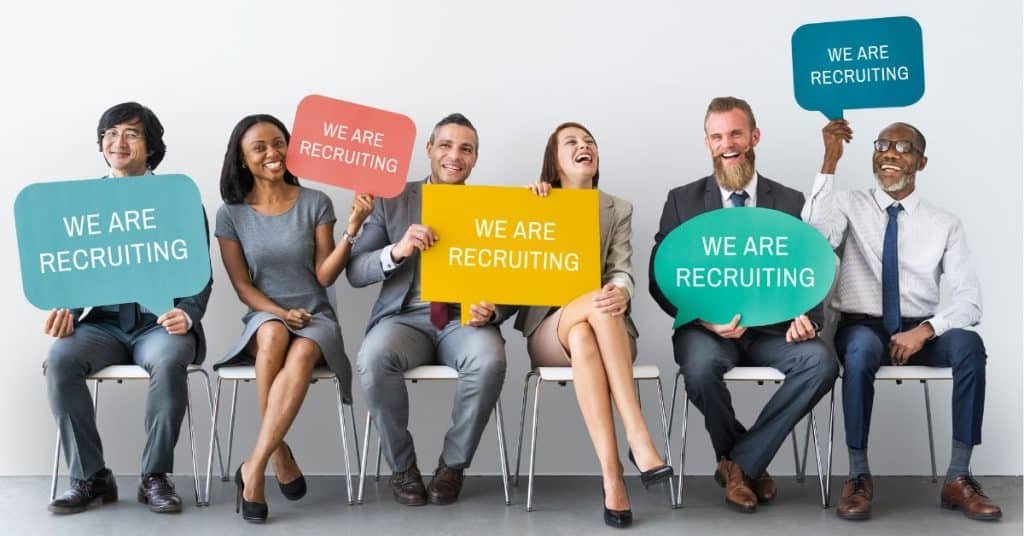 Diverso equipo de reclutadores sosteniendo carteles de "We Are Recruiting" - Kilpatrick Executive Search
