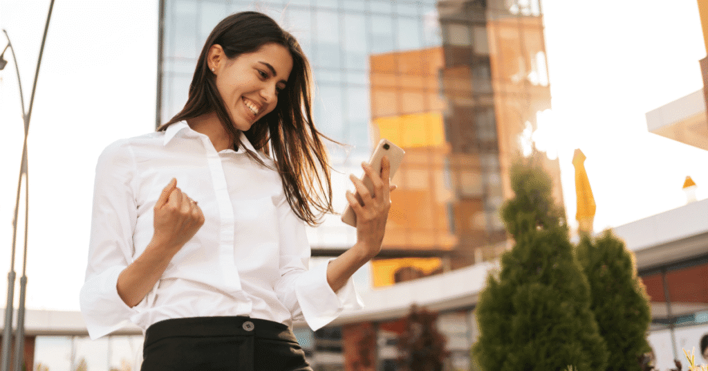 Smiling businesswoman celebrating with phone — financial literacy and pay transparency in executive hiring | Kilpatrick