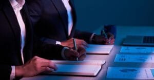 Ejecutivos en sesión de compliance empresarial tomando notas junto a gráficos financieros, representando la estrategia de cumplimiento en México con Kilpatrick.