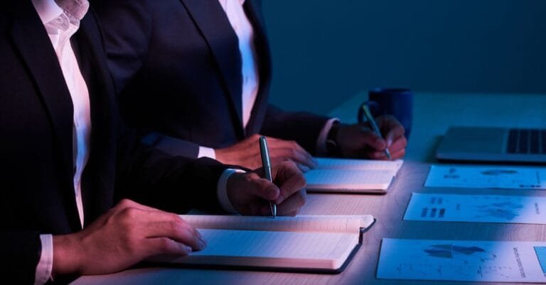 Ejecutivos en sesión de compliance empresarial tomando notas junto a gráficos financieros, representando la estrategia de cumplimiento en México con Kilpatrick.